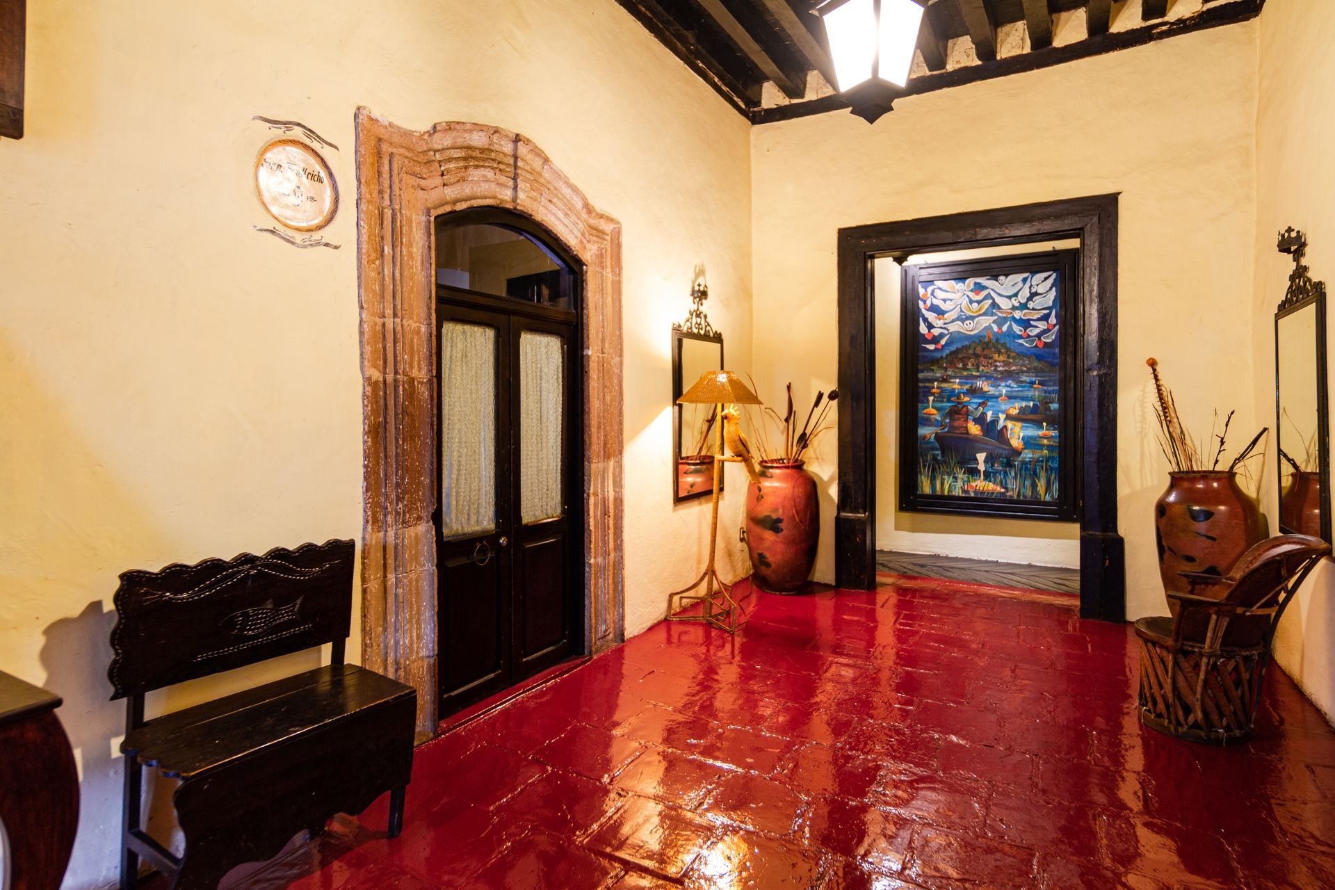 A hallway with red floors, cream walls, and dark wood accents. Features include a doorway, artwork and furniture.