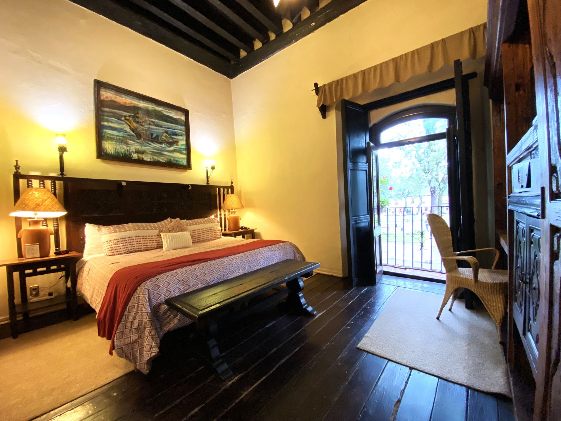 Bedroom with dark wood furniture, bed, and balcony. Walls are light-colored; doorway and ceiling are dark.