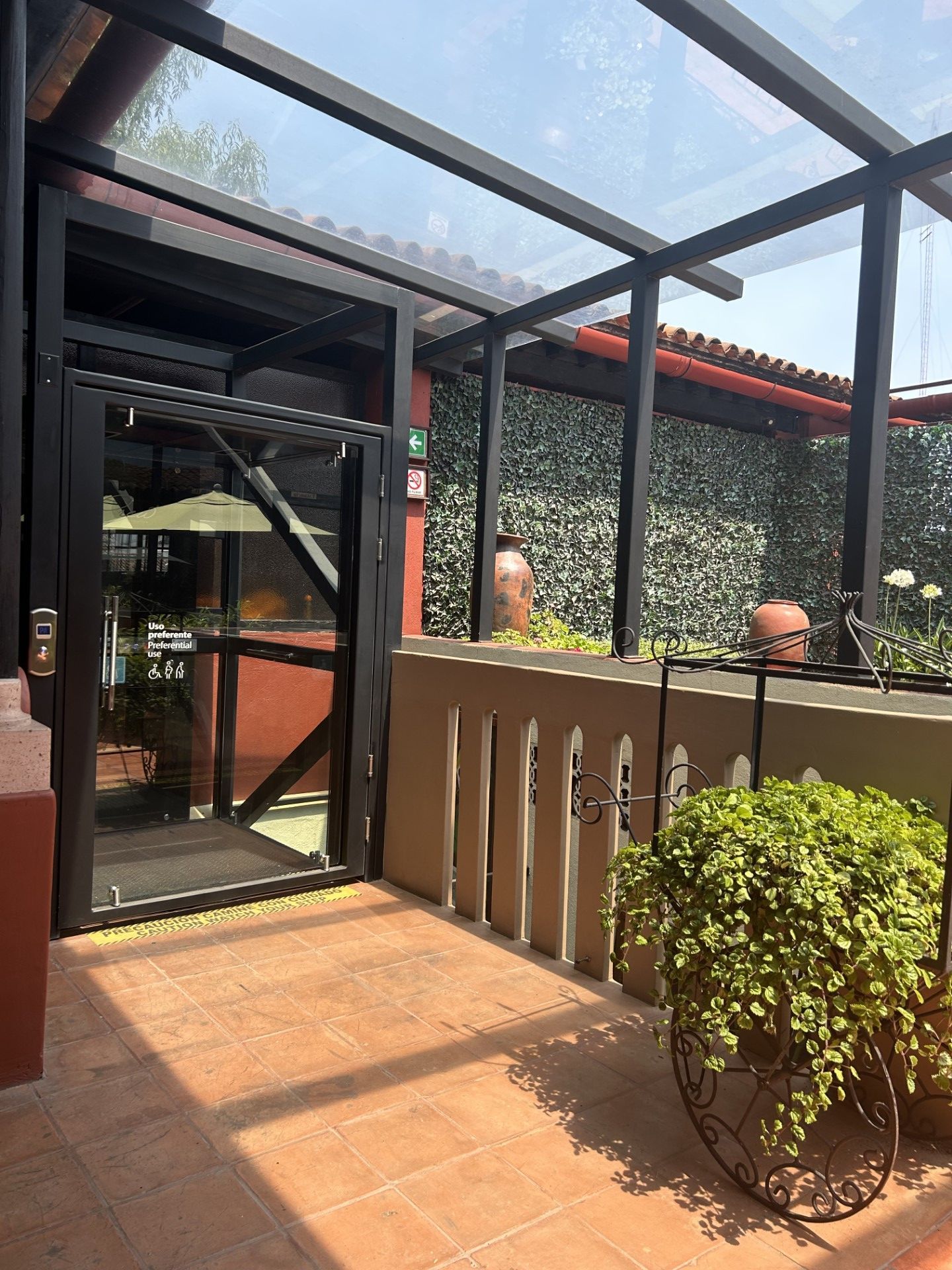 Terrace with glass roof and door, tiled floor, potted plants, and a decorative wall with stucco.