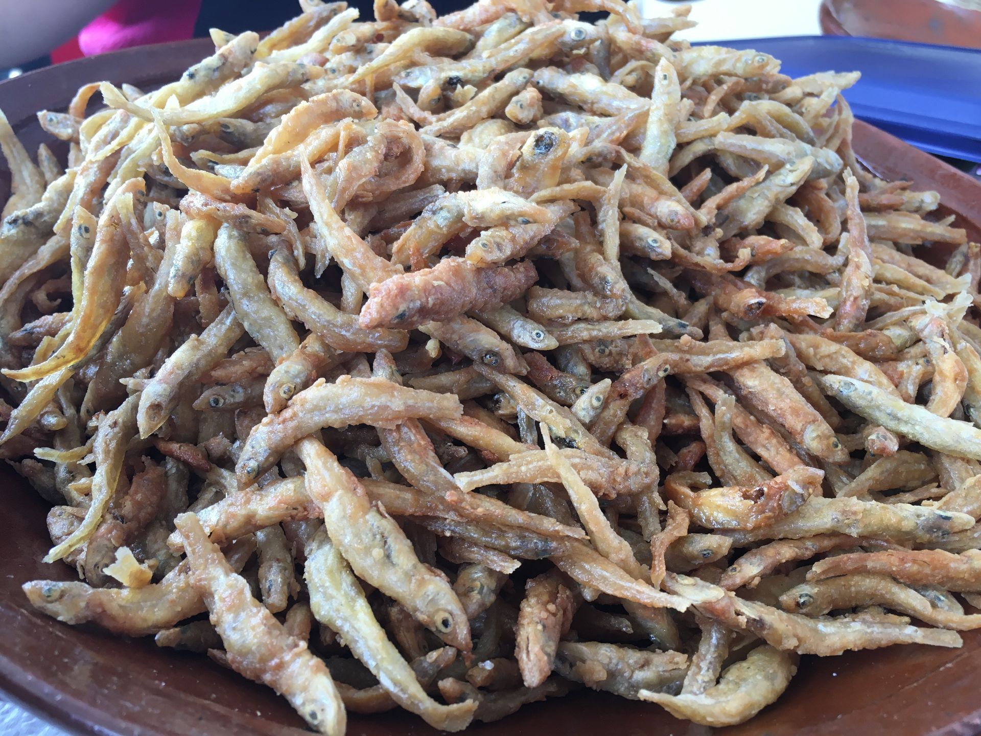 Pile of fried small fish on a brown plate; golden-brown and crispy.