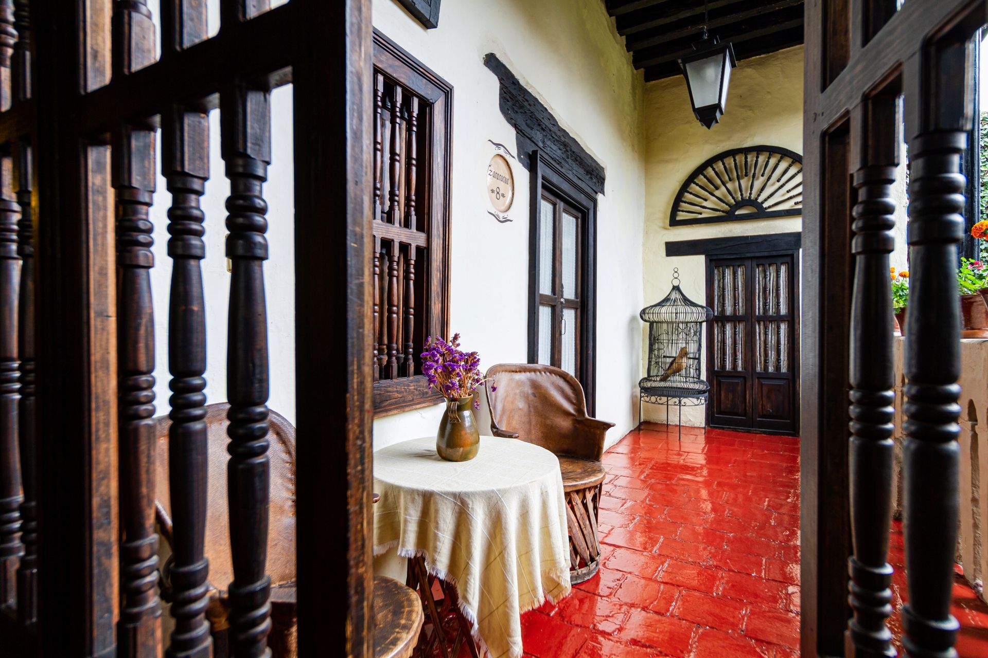 Balcony with red tile floor, white walls, and dark wood trim. A small table with a floral centerpiece sits near chairs.