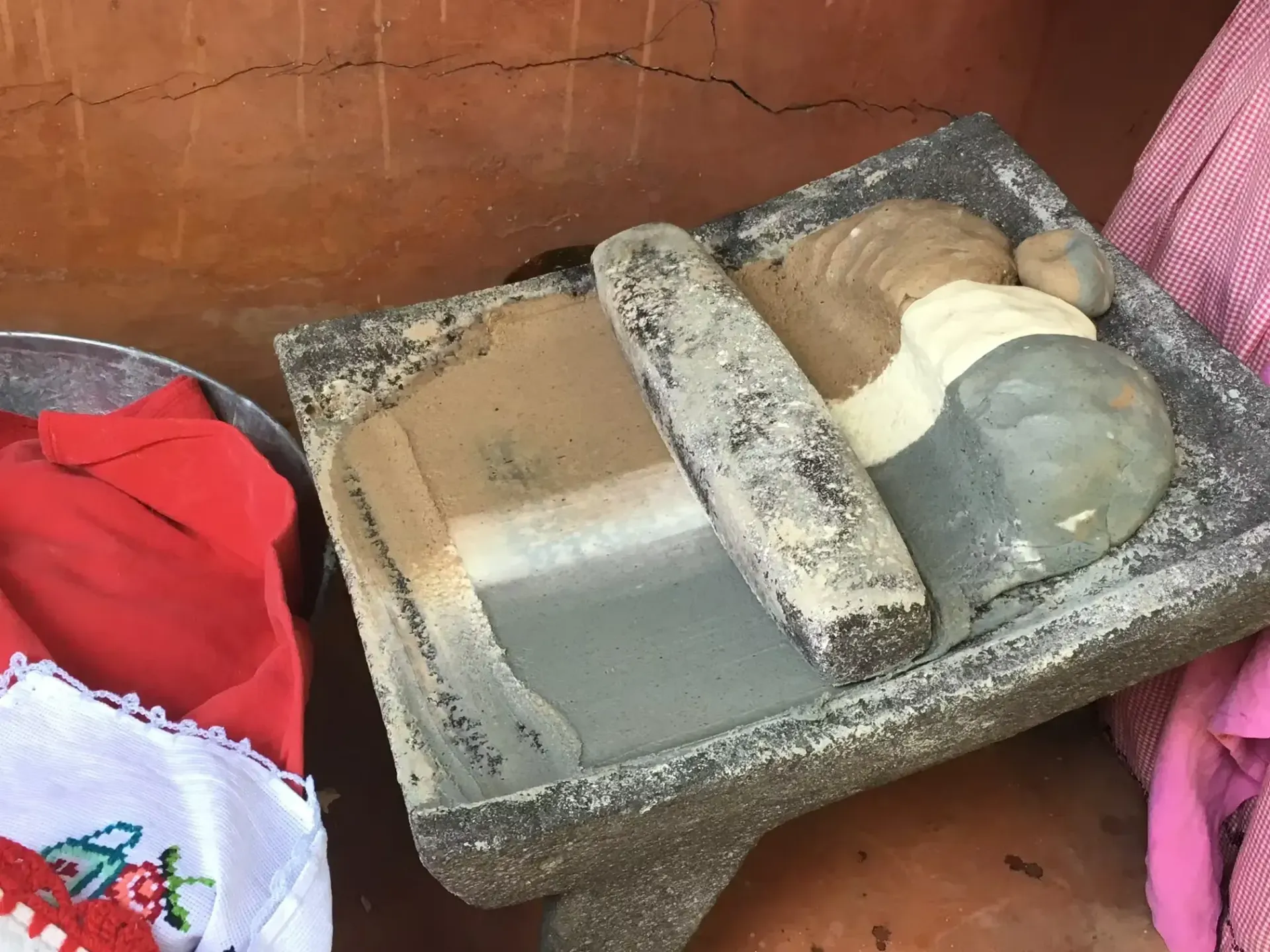 A molcajete (Mexican mortar and pestle) with contents, beside red clothing. Located in a rustic setting.