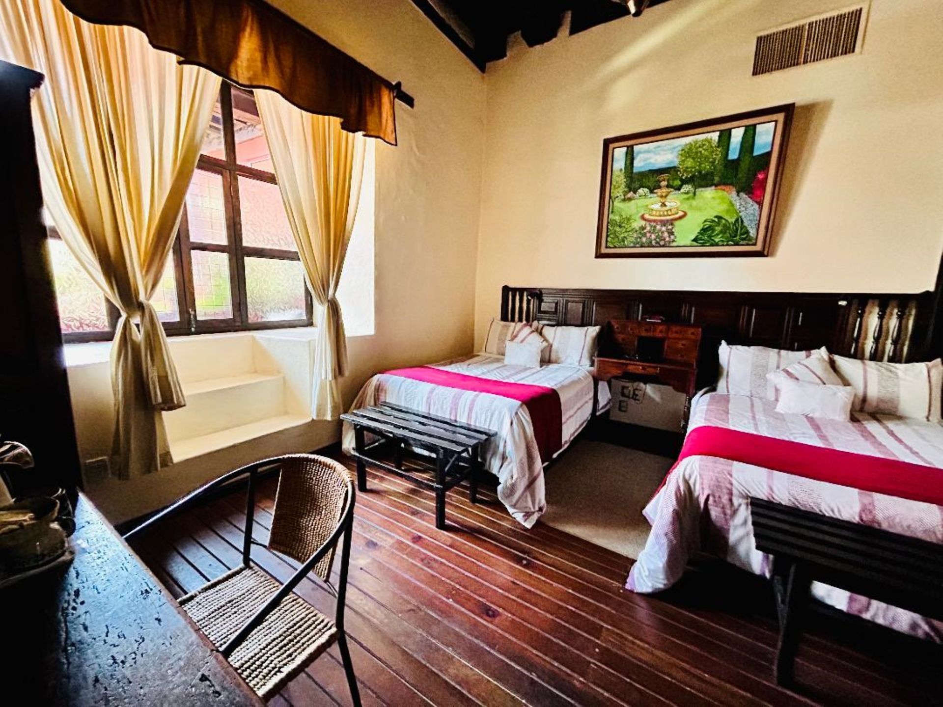 Bedroom with two twin beds, wooden floors, and a window with curtains. A painting hangs above the beds.
