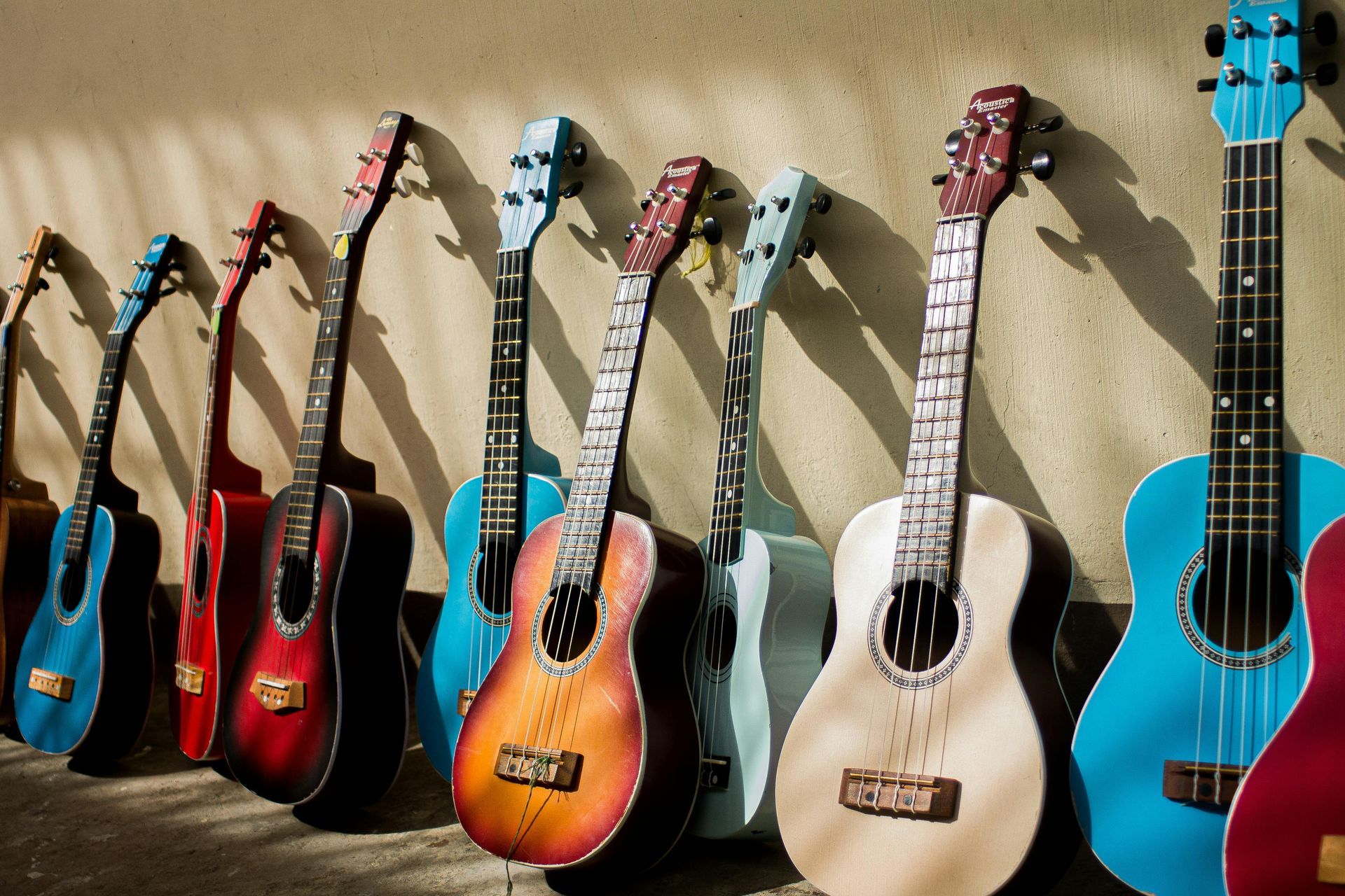 Row of colorful ukuleles leaning against a textured wall. The instruments vary in color.