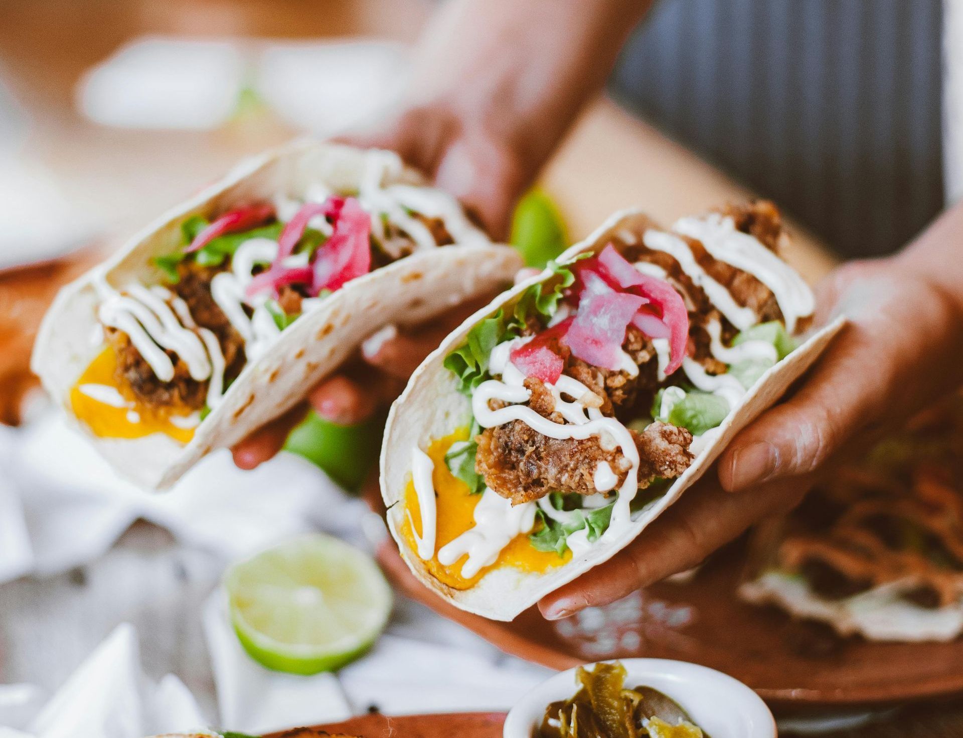 Person holding two tacos filled with meat, lettuce, sauce, and pickled onions.
