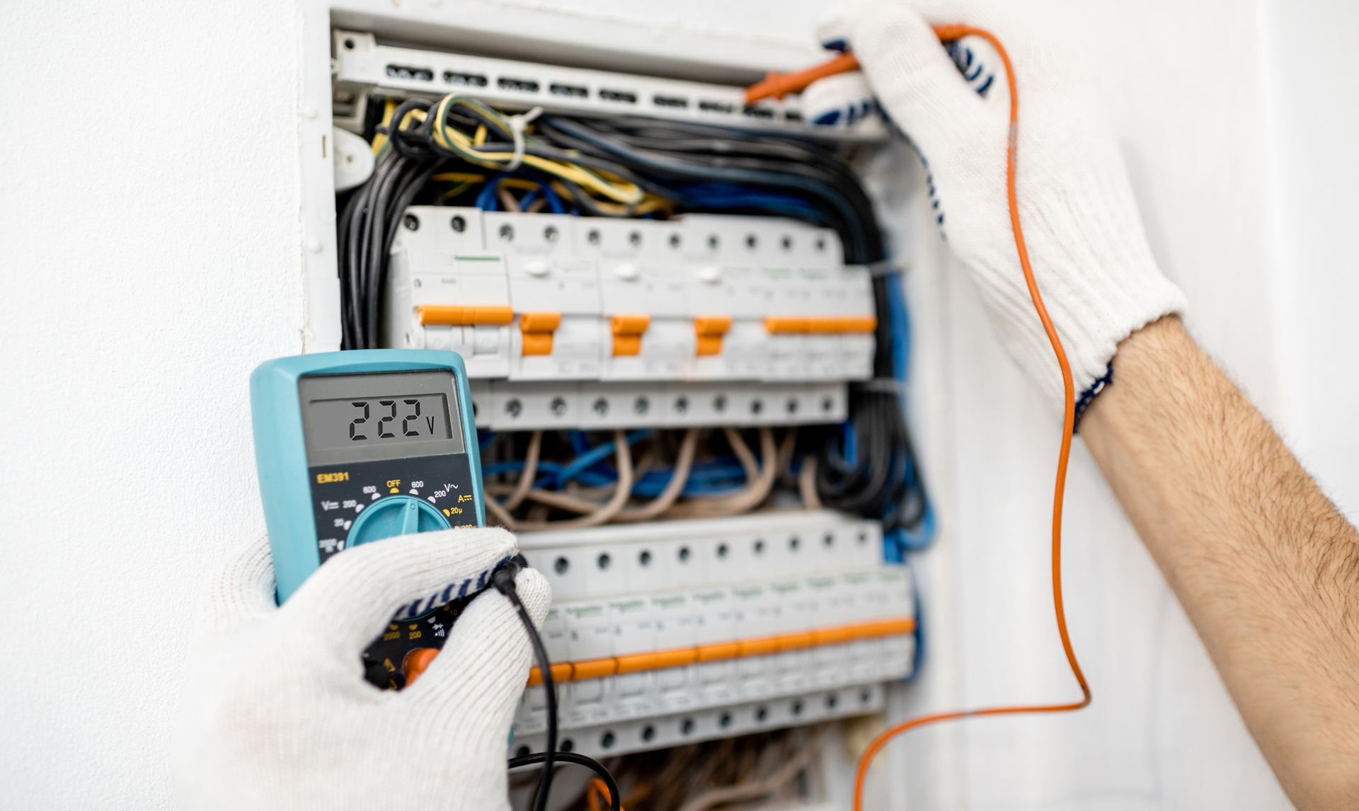 Electrician using a multimeter to test a fuse box; showing 222 volts.