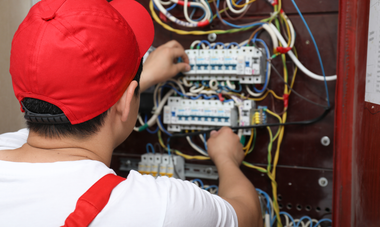 Electrician in red cap and white shirt working on electrical panel, wiring.