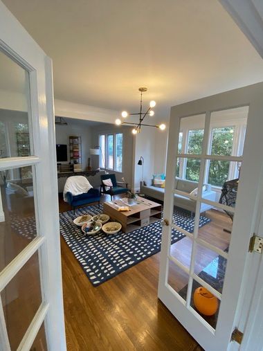Open doorway leads to a living room with blue and white rug, sofas, coffee table, and large windows.