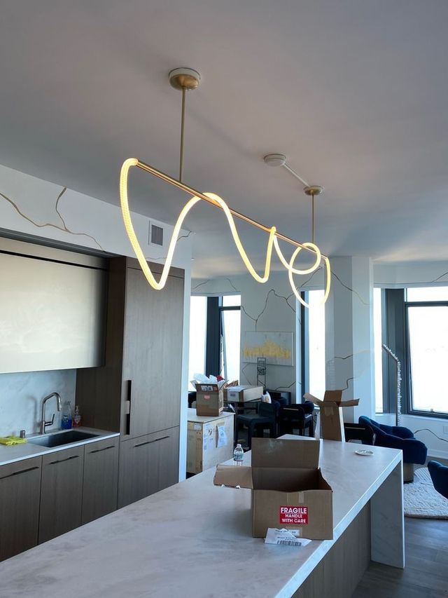 Modern kitchen with gold wavy light fixture above a white island.