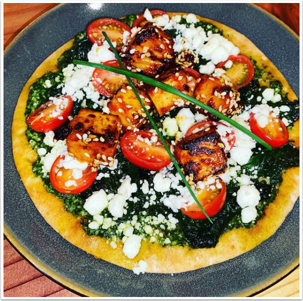 A pizza with spinach tomatoes and cheese on a plate