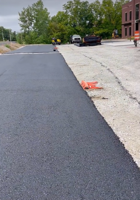 A black asphalt road is being built next to a building.