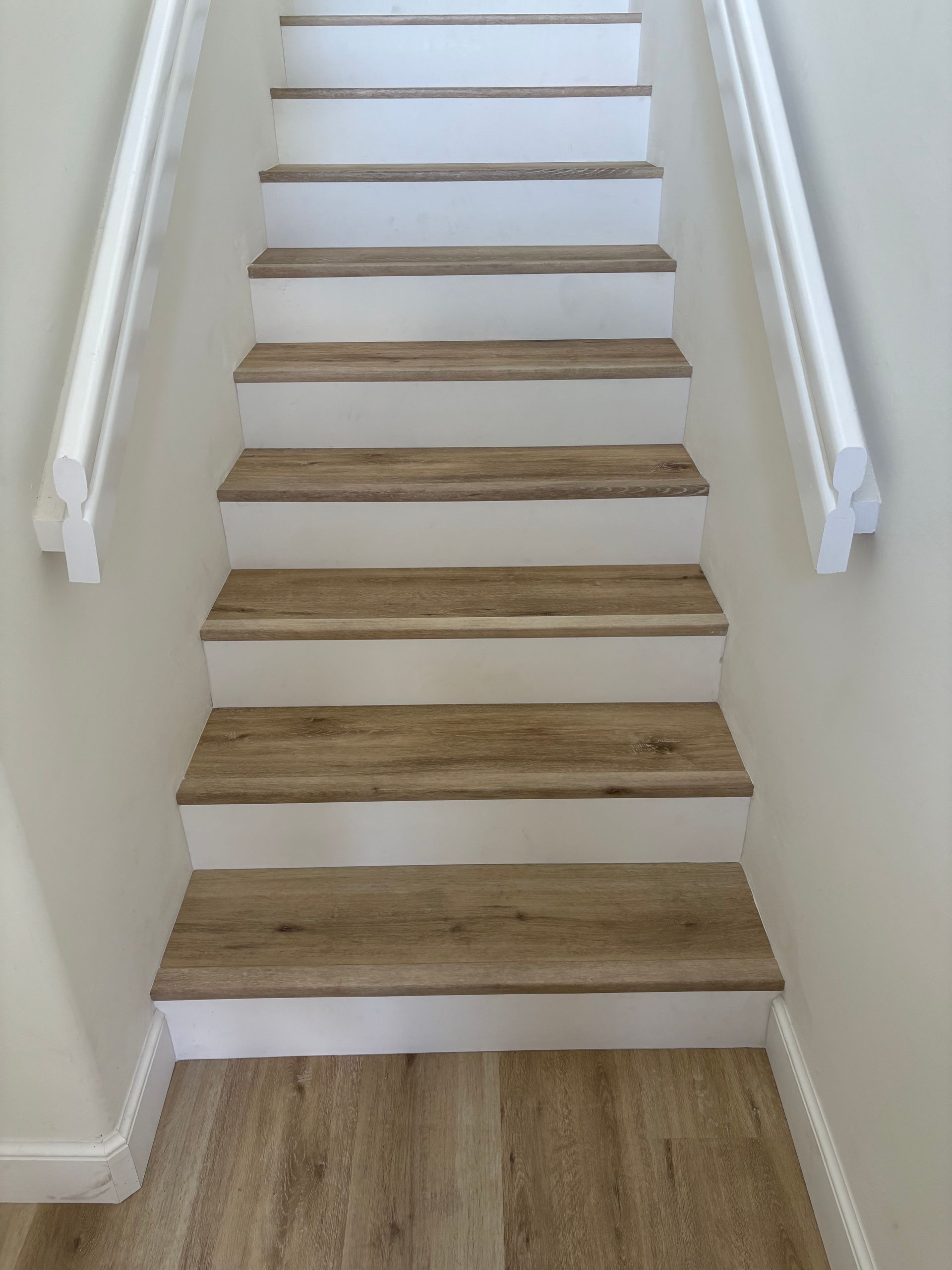 Staircase with wood-look treads and white risers, banisters on both sides. Flooring at the bottom matches the stair treads.