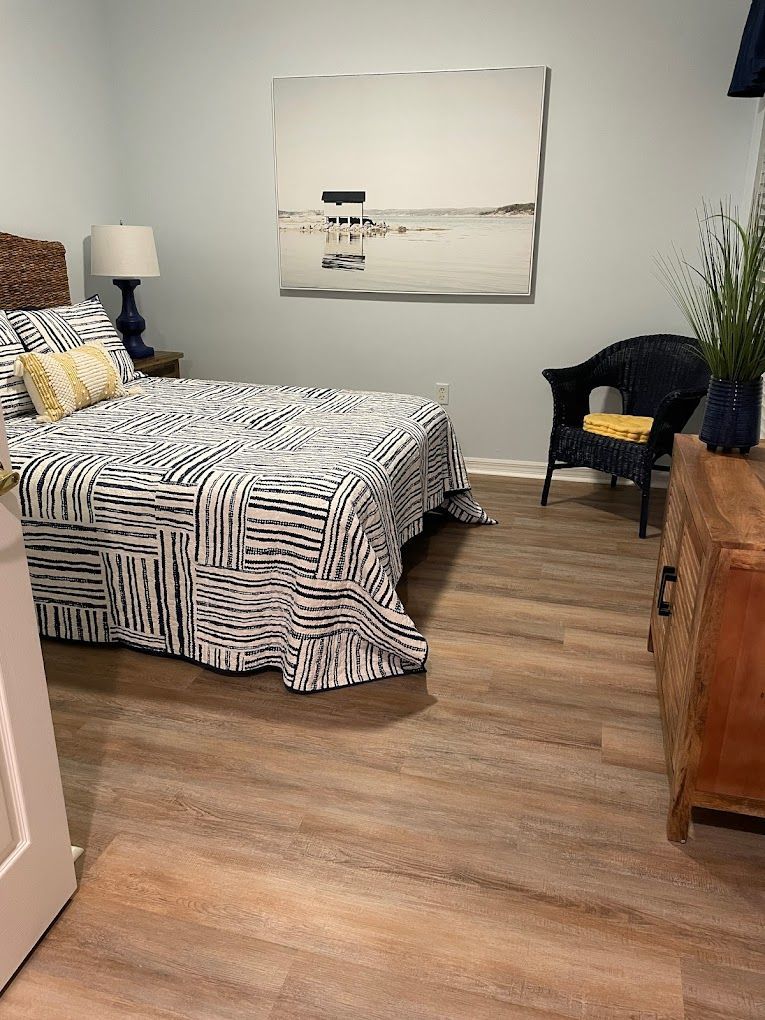 A bedroom with a bed , chair , dresser and painting on the wall.