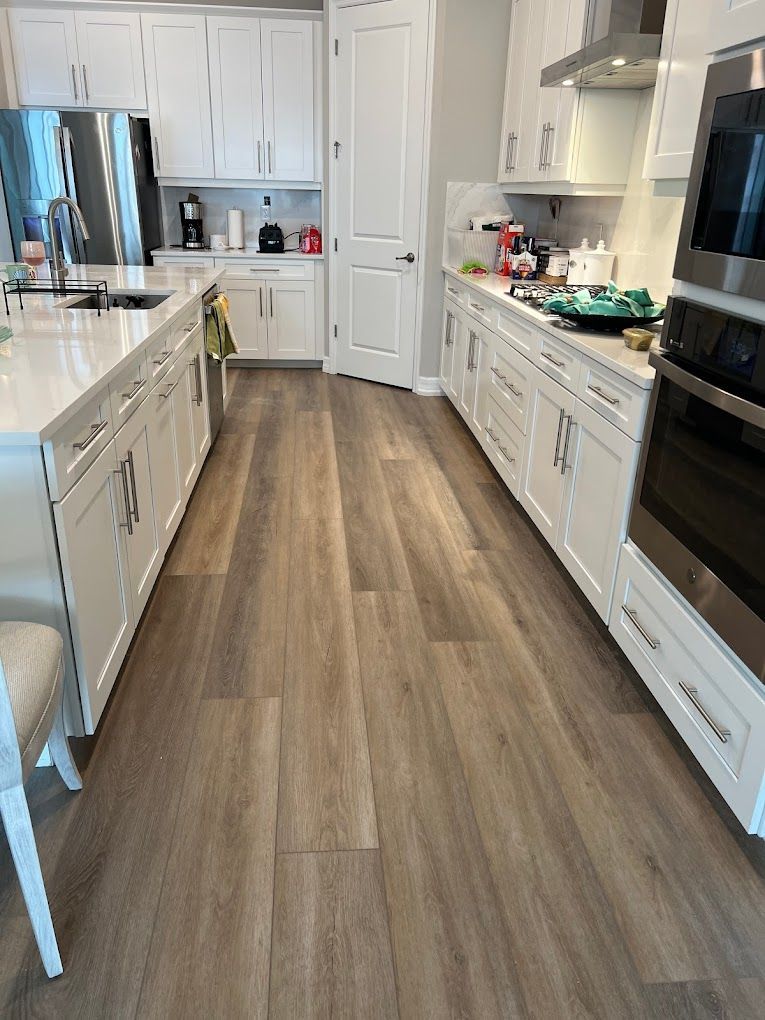 A kitchen with hardwood floors , white cabinets , stainless steel appliances and a large island.