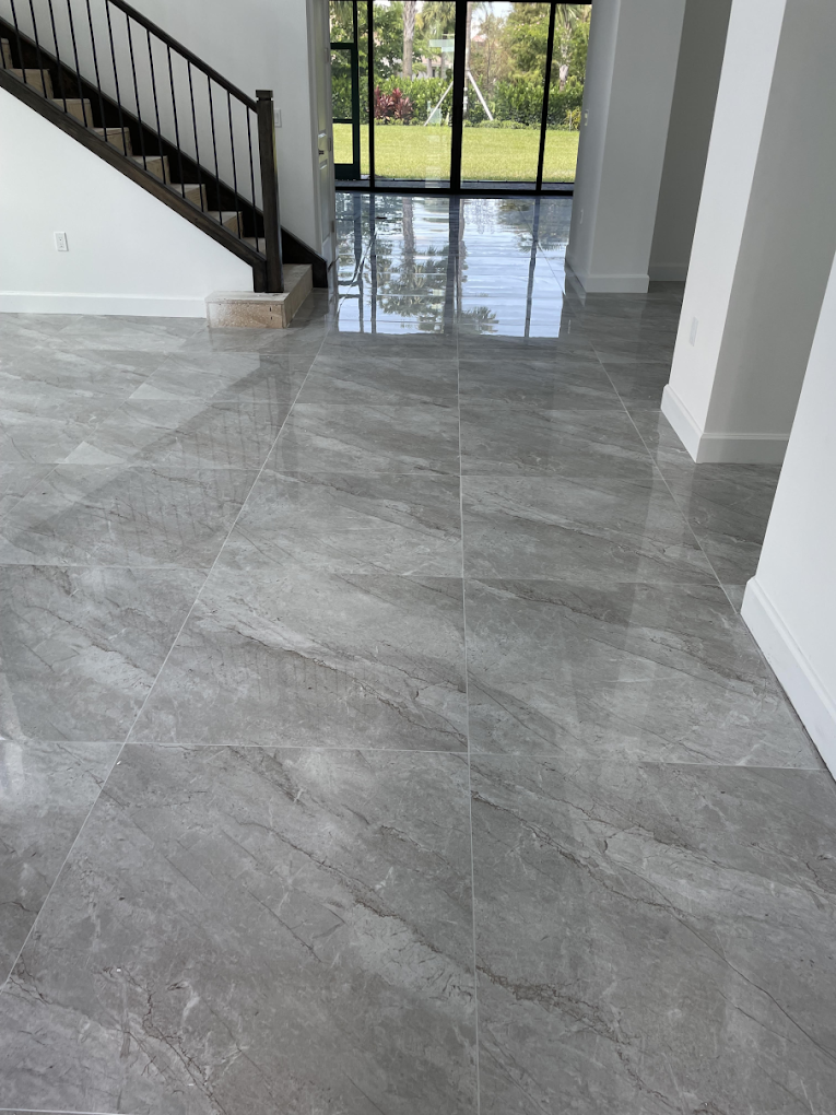 Gray marbled tile floor reflecting light in a modern home with stairs and glass doors.