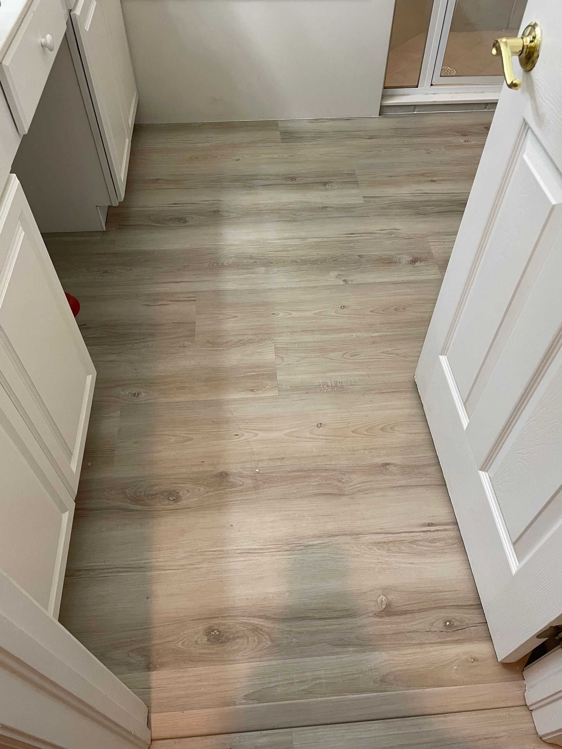 View of a room with light wood-look flooring and white cabinets. A white door is open on the right.