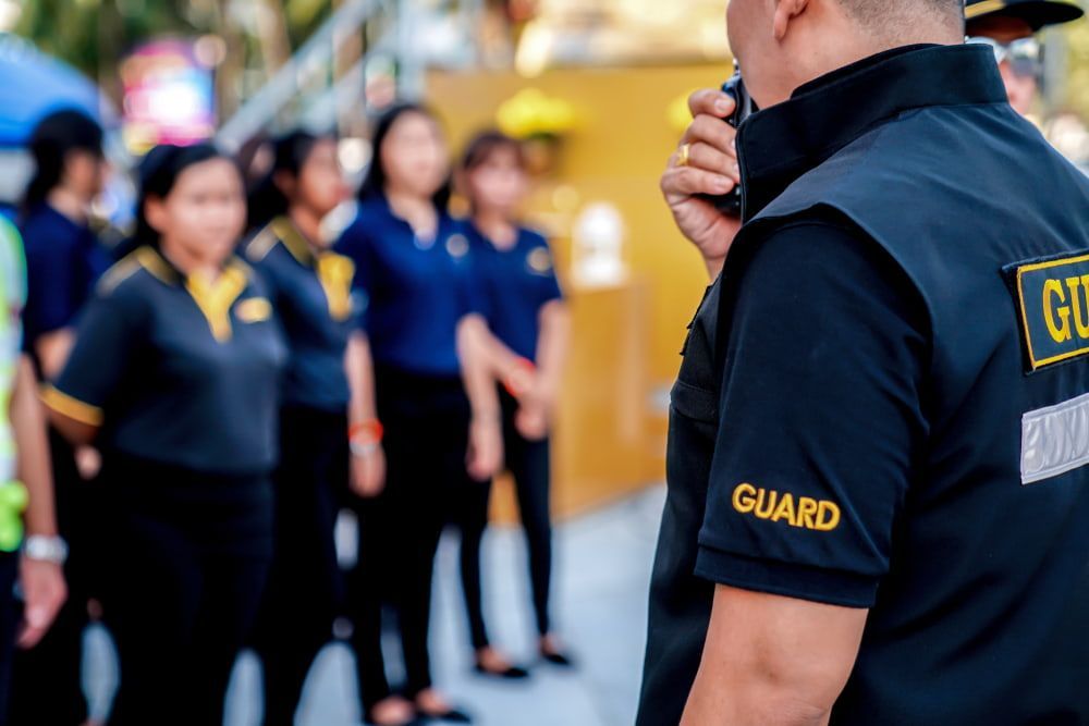 A Man Is Talking On A Walkie Talkie In Front Of A Group Of People - Comprehensive Security Services in Darwin, NT