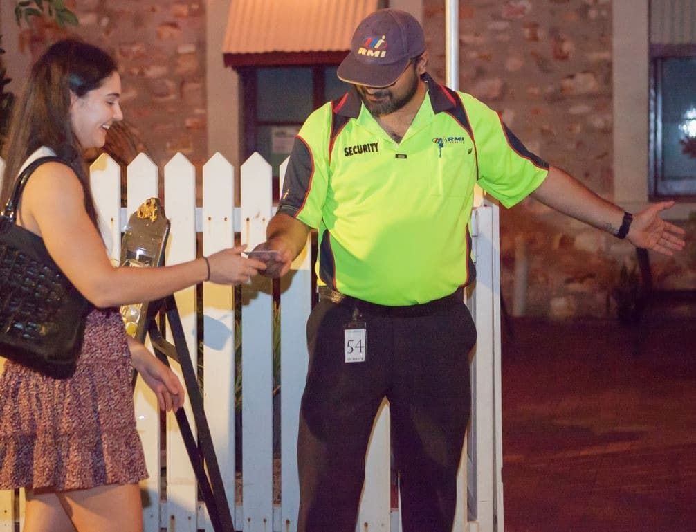 A Woman Hands Her Id to a Smiling Security Guard Wearing a Bright Yellow Shirt