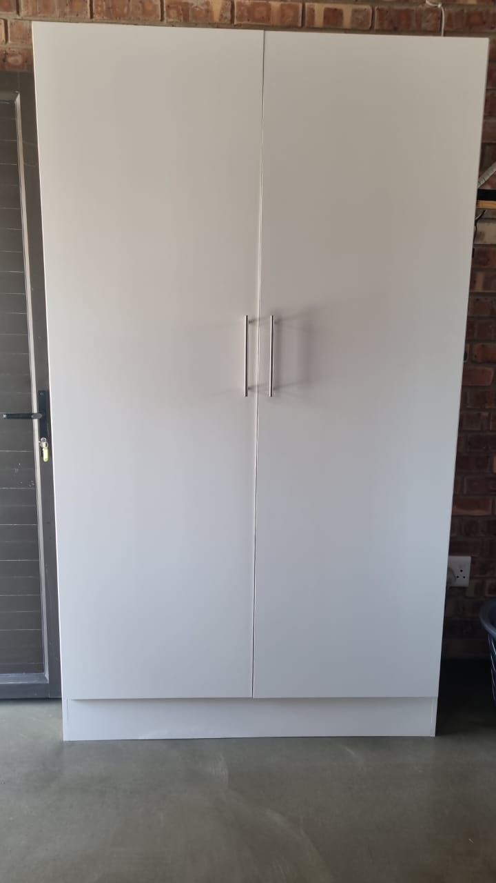 A white cabinet with two doors is sitting in a room next to a brick wall.