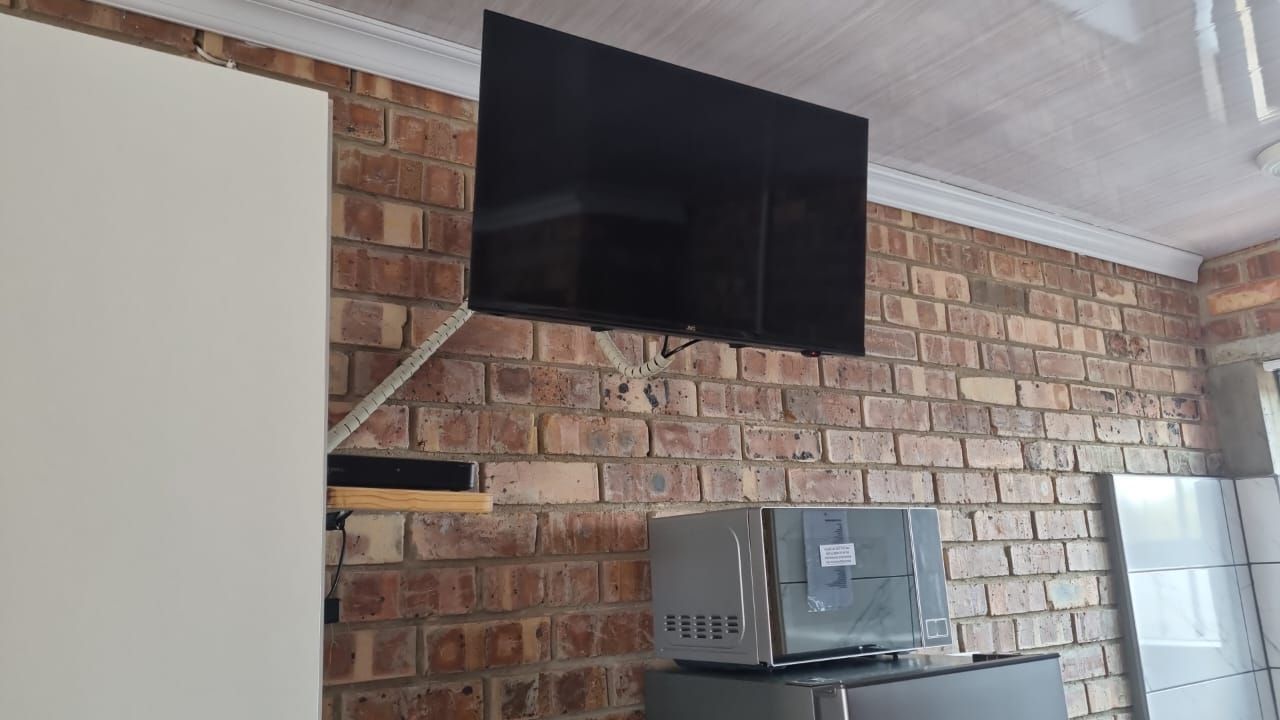 A flat screen tv is hanging from the ceiling in a kitchen.