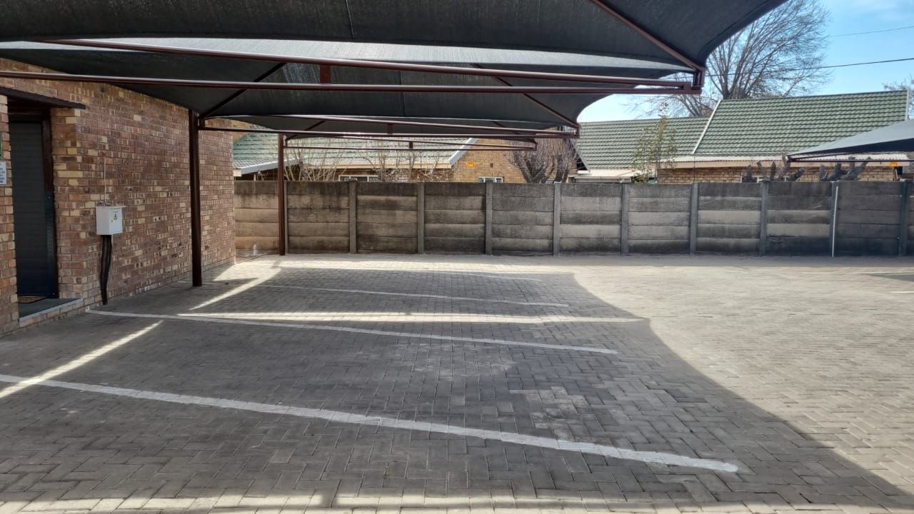 A parking lot with a brick building and a fence in the background.