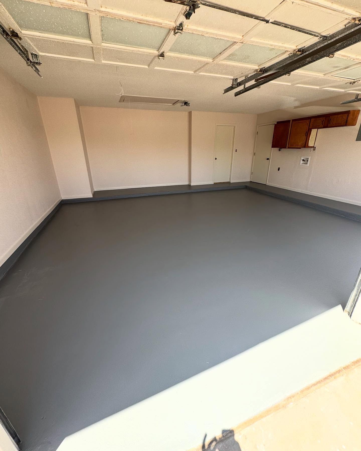 Empty garage with gray floor and beige walls. Ceiling with white panels and garage door opener.