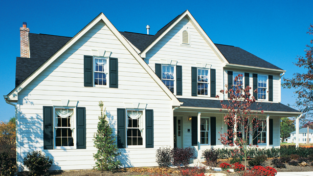 White house with black shutters, front porch, and dark roof under a blue sky.