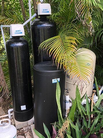 Three black water filters are sitting next to each other in a garden.