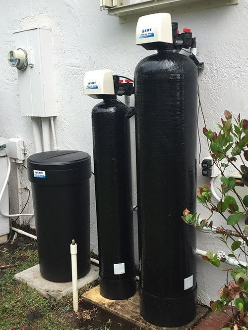 Two black water filters are sitting next to each other outside of a house.