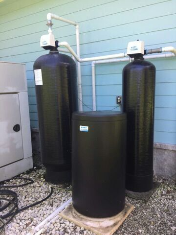 Two black water tanks are sitting next to each other in front of a house.