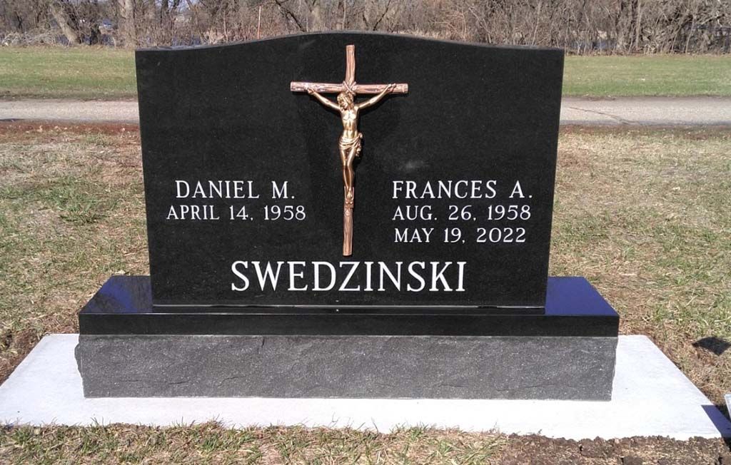 Black gravestone with crucifix and the name SWEDZINSKI in a cemetery
