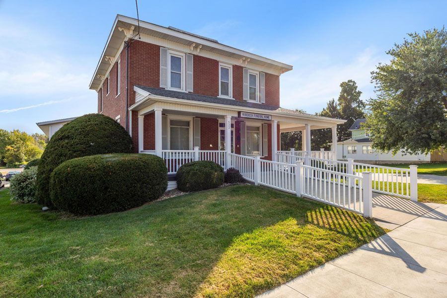 A red brick house with a white porch and a white fence.