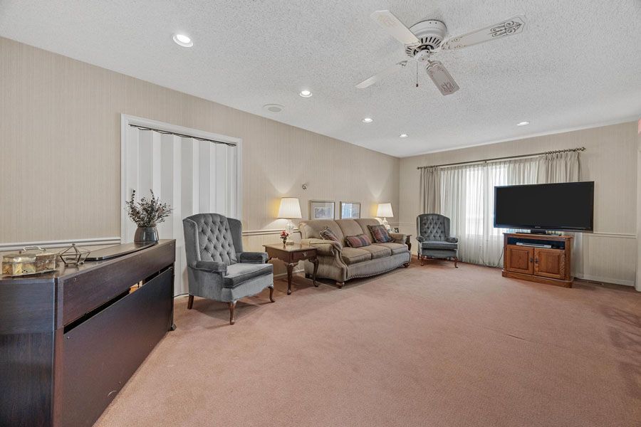 A living room with a couch , chairs , a television and a ceiling fan.