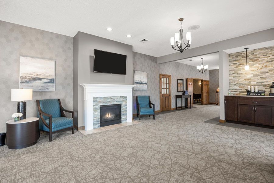 A living room with a fireplace , chairs , a television and a chandelier.
