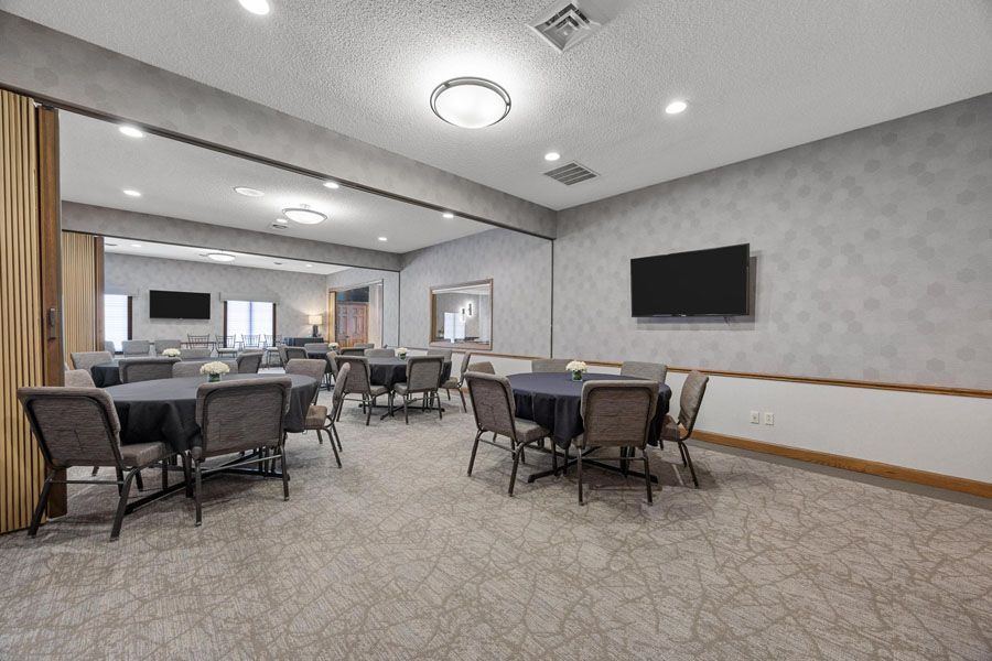 A large room with tables and chairs and a flat screen tv on the wall.