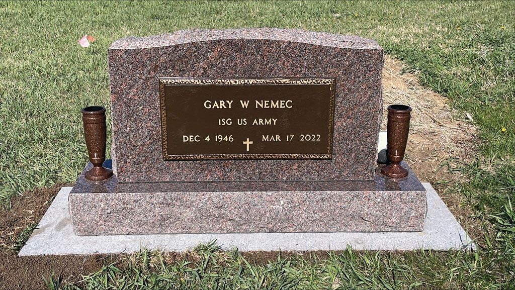 Gravestone with bronze plaque and two vases on a grassy cemetery plot