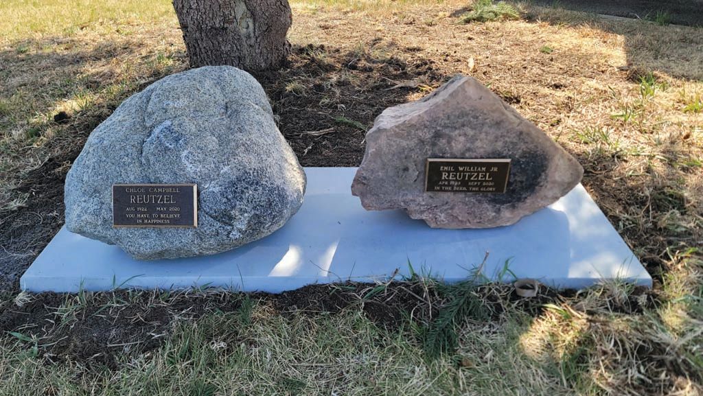 Two engraved memorial rocks on a white slab in a grassy outdoor area