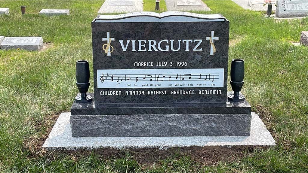 Black granite gravestone with “VIERGUTZ” engraved, flanked by small lamps, in a cemetery
