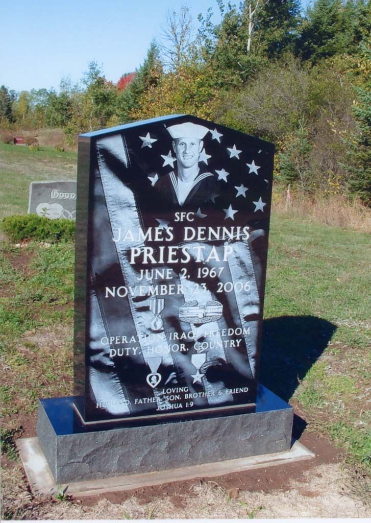 Black gravestone with star design in a sunny cemetery, set on a concrete base with trees in the background
