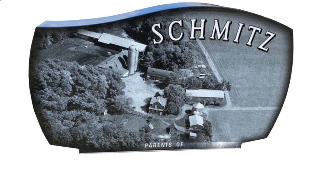 Black-and-white scenic sign with “SCHMITZ” over a hillside cabin and trees