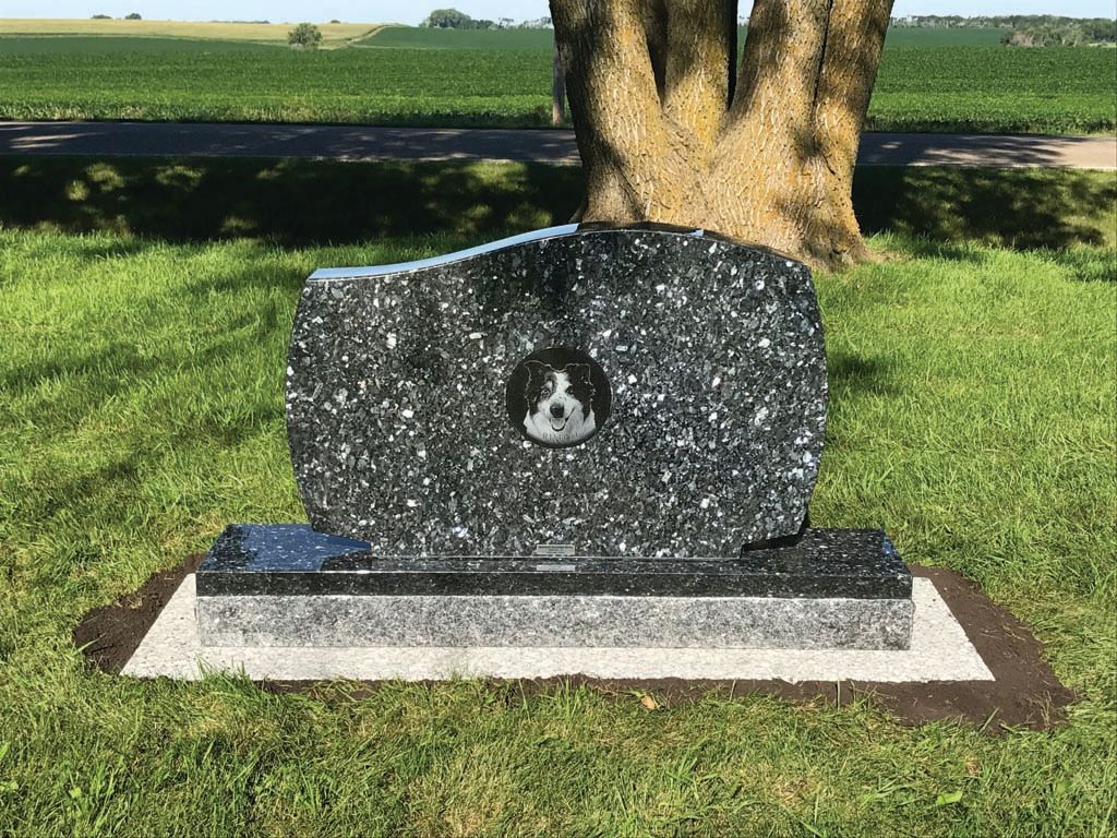Granite memorial stone on a lawn with a tree and roadside in the background