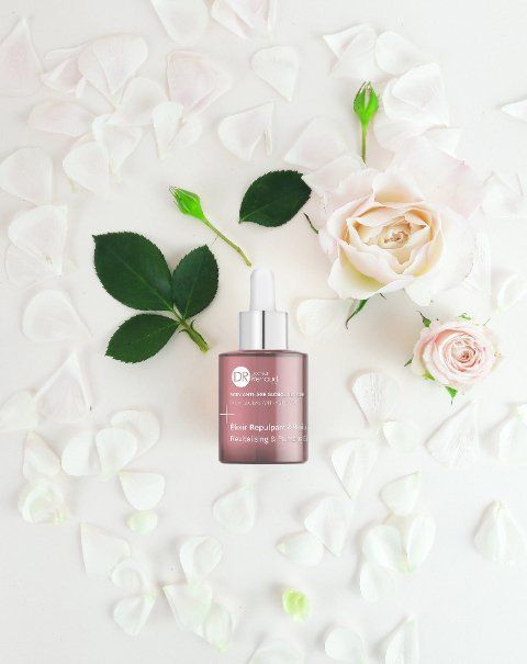 Een flesje parfum is omringd door rozen en bloemblaadjes op een wit oppervlak.