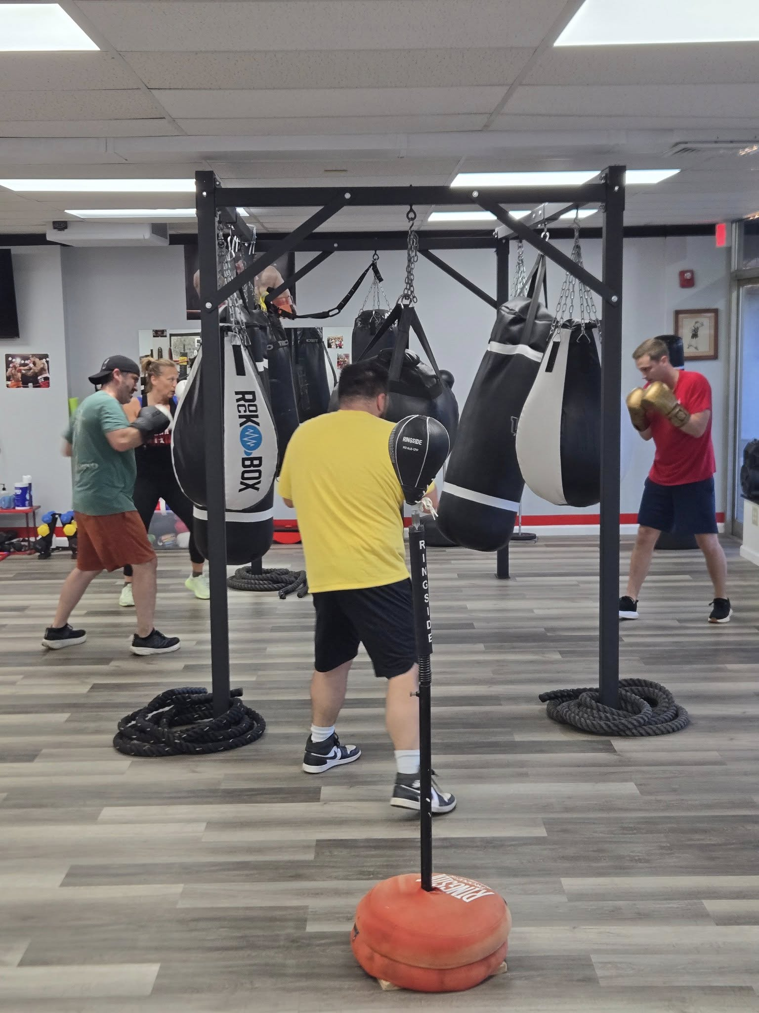 People boxing in a gym, hitting hanging bags and a freestanding target.