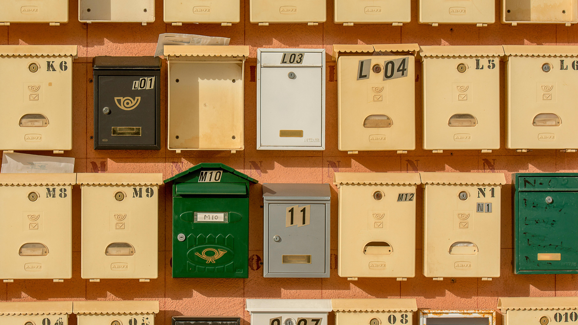 Wall of mailboxes, various colors and styles, with numbers, set against a peach-colored wall.