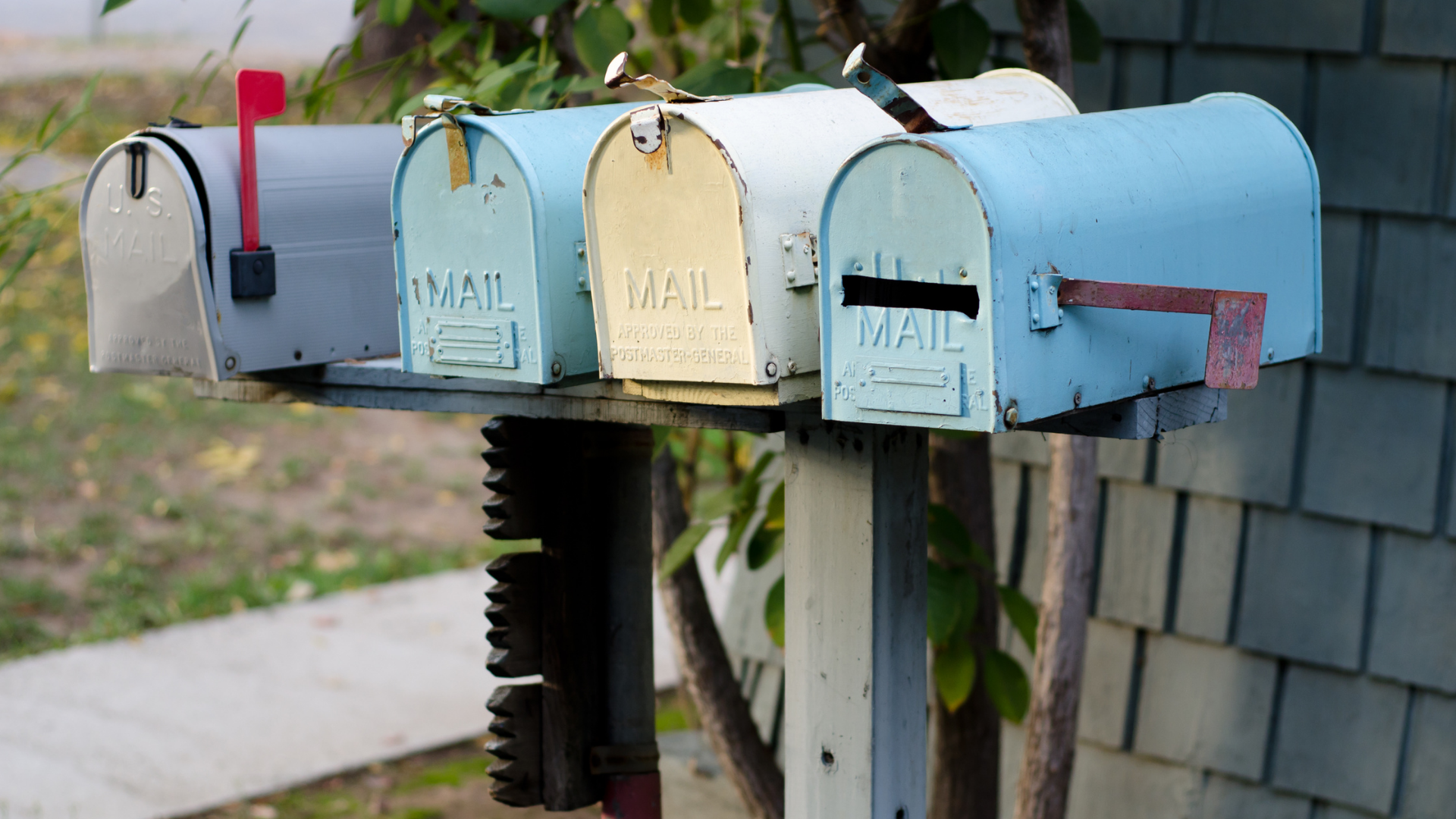 Five weathered mailboxes of varying colors.