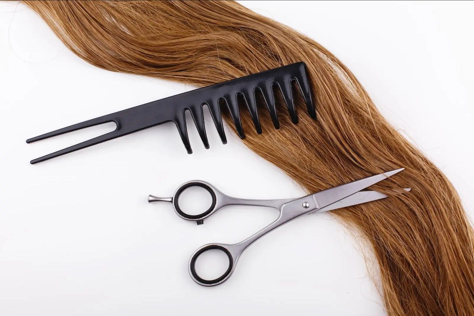 A comb and scissors are sitting on top of a piece of hair.