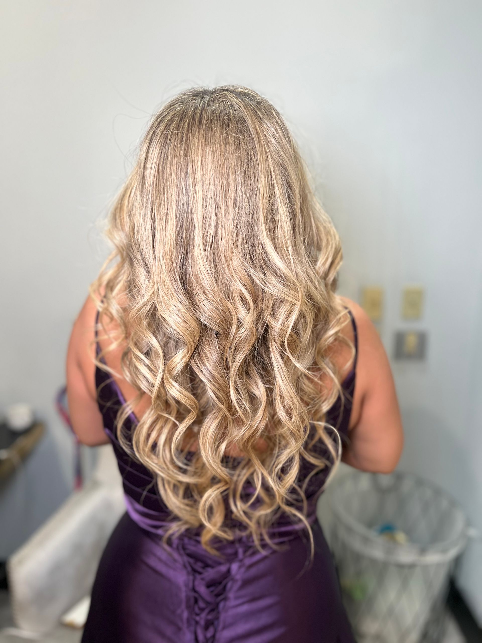 The back of a woman in a purple dress with blonde curly hair.