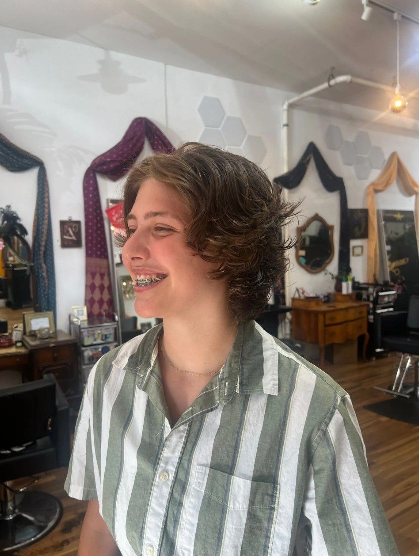 Person smiling in a salon, short layered brown hair, striped green and white shirt.