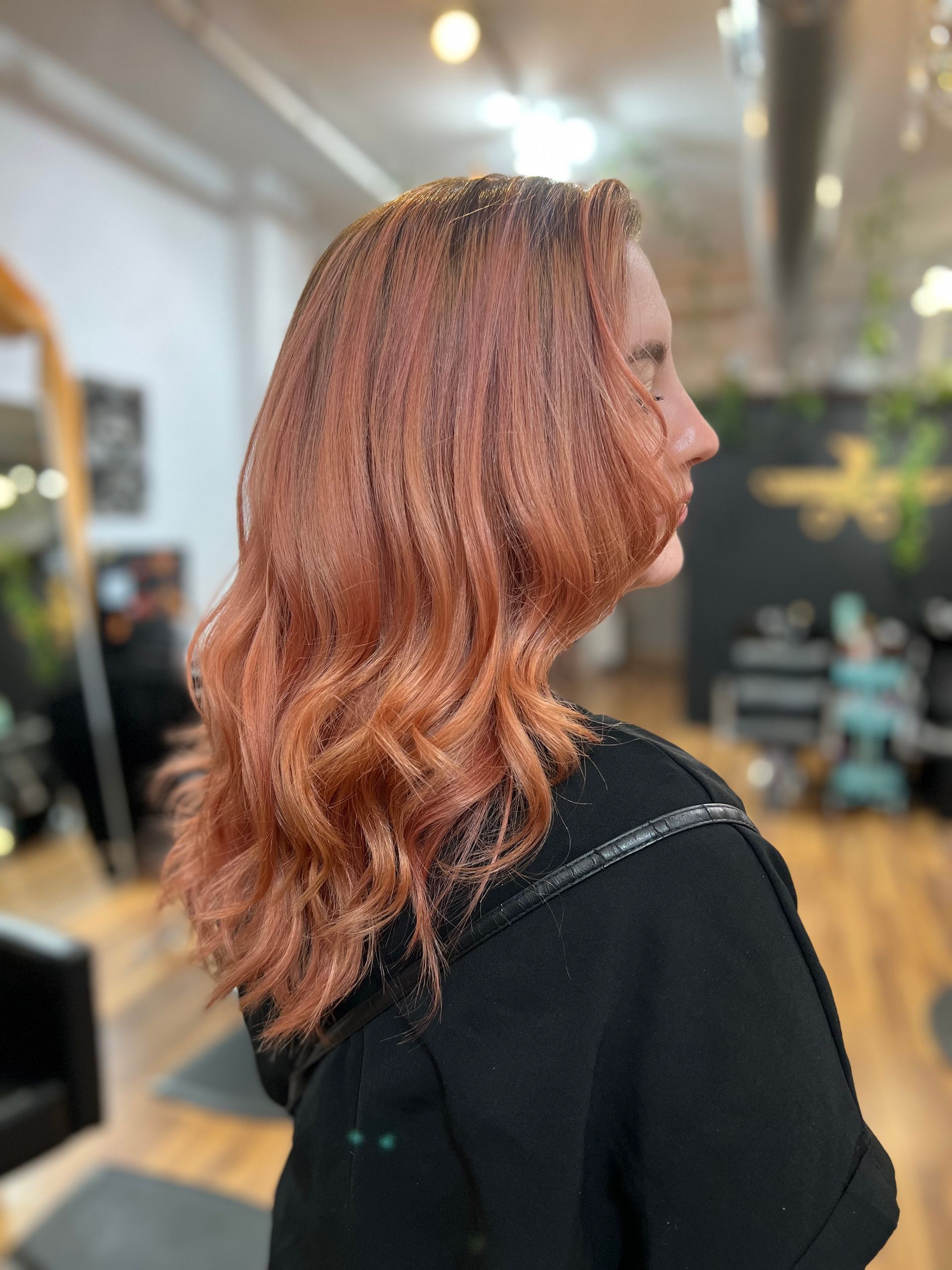 A woman with long red hair is standing in a salon.