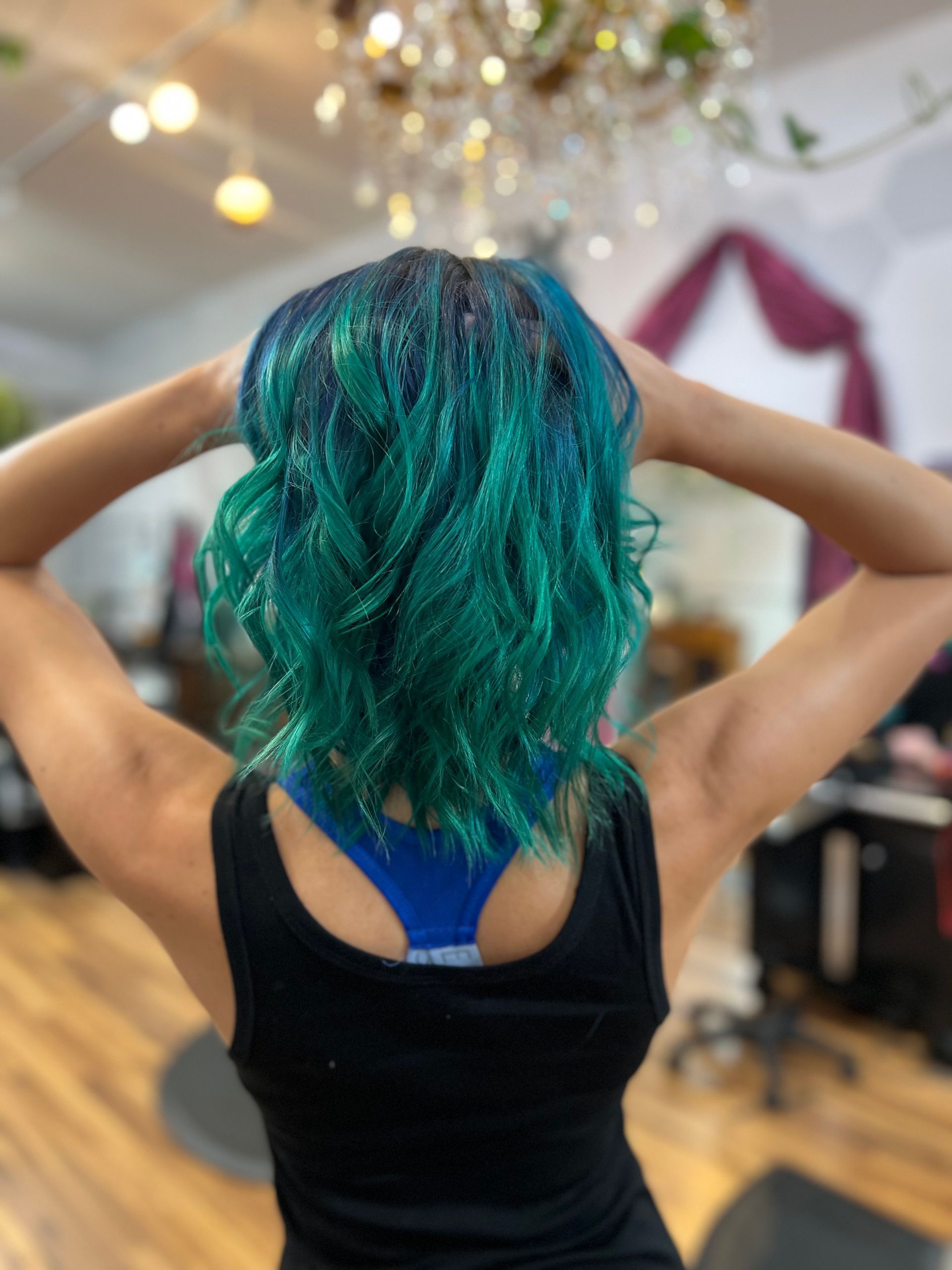 A woman with green hair is standing in a room with her hands behind her head